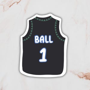 May include: A black sleeveless jersey featuring a dark green patterned trim along the neckline and armholes. The word BALL is printed in white with a light blue outline above the number 1, which is also in white with a light blue outline.