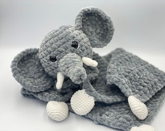 May include: A gray crocheted elephant plush toy with white crocheted accents. The elephant is attached to a gray crocheted blanket.