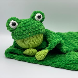 May include: A green crocheted frog plush toy with white eyes and a green crocheted blanket.