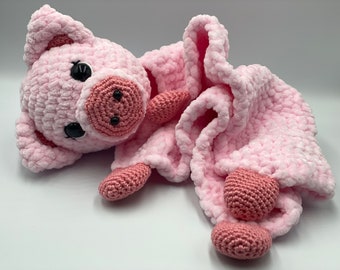 May include: A pink crocheted pig with black eyes and a pink blanket. The blanket has three pink crocheted balls attached to it.