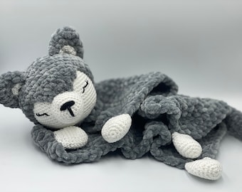 May include: A gray crocheted stuffed animal with a white face and closed eyes, lying on a gray crocheted blanket.