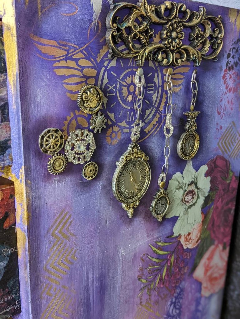 Może przedstawiać: Purpurowa i złota ozdobna skrzynka z kwiatowym wzorem i r&oacute;żnymi metalowymi ozdobami, w tym tarczą zegara, kołami zębatymi i łańcuchami.
