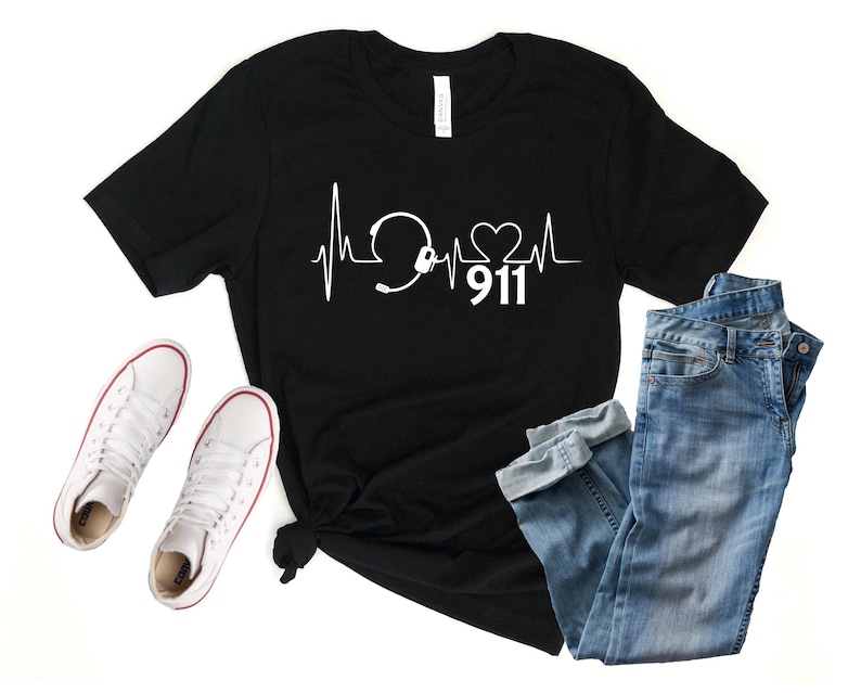 May include: Black t-shirt with a white graphic of a heartbeat with a headset and a heart, and the number 911.