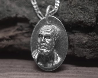 May include: A silver pendant necklace featuring a detailed portrait of a man with a beard. The pendant is oval-shaped and hangs from a silver chain.