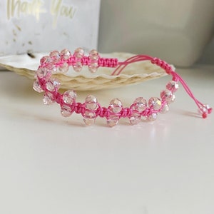 May include: Pink crystal beaded bracelet with a pink cord. The bracelet is tied with a knot and has a tassel.