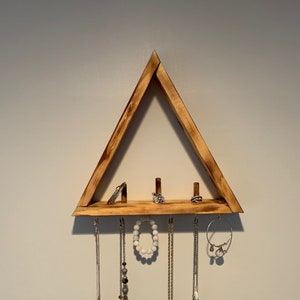 May include: Wooden triangle shelf with five hooks for hanging necklaces and bracelets. The shelf has a natural wood finish and is mounted on a white wall.