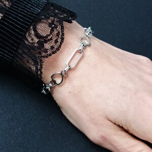 May include: A silver bracelet with a chain link design featuring alternating heart and rectangular shapes.