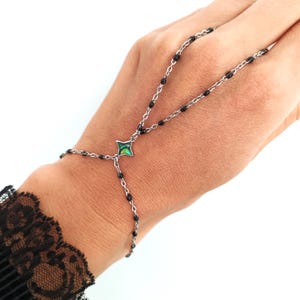 May include: A silver chain bracelet with black beads and a green and blue abalone shell charm. The bracelet is designed to be worn on the wrist and finger.
