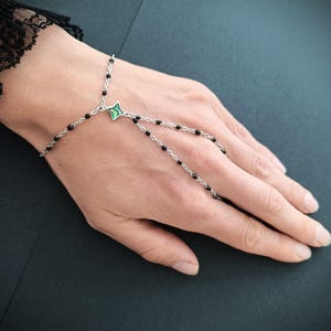 May include: A silver chain bracelet with black beads and a green and silver star charm. The bracelet is designed to be worn on the wrist and finger.