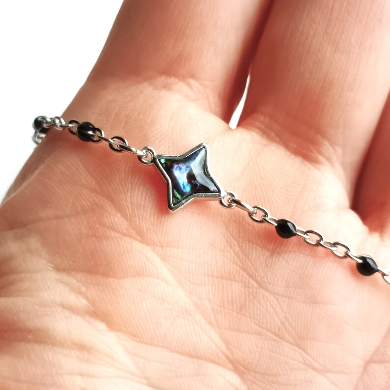 May include: A silver chain bracelet with black beads and a star-shaped charm. The charm is made of iridescent abalone shell.