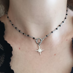 Puede incluir: Un collar de cadena plateada con detalles de cuentas negras y un colgante en forma de estrella.