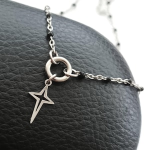 Puede incluir: Un collar de cadena de plata con cuentas negras y un colgante en forma de estrella. La cadena tiene un cierre de anillo de plata.