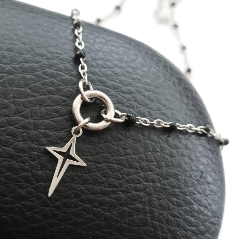 Puede incluir: Un collar de cadena de plata con cuentas negras y un colgante en forma de estrella. La cadena tiene un cierre de anillo de plata.