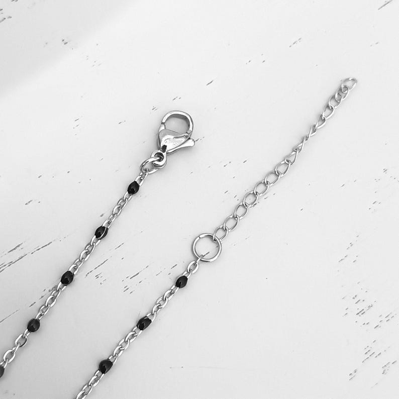 Puede incluir: Un collar de cadena plateada con cuentas negras. El collar tiene un cierre de langosta y una cadena extensora.