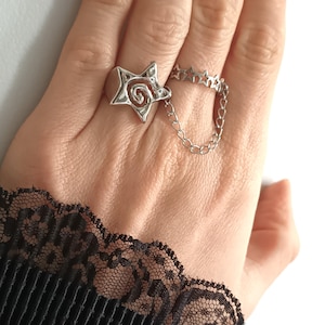 May include: A silver ring featuring a star design with a chain attached. The chain connects to a second ring with a row of stars.
