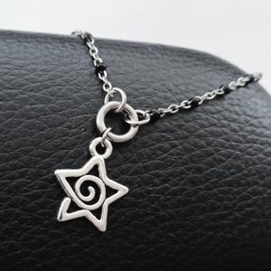 Puede incluir: Un collar de cadena de plata con un acento de cuentas negras y un dije de estrella con un dise&ntilde;o en espiral.