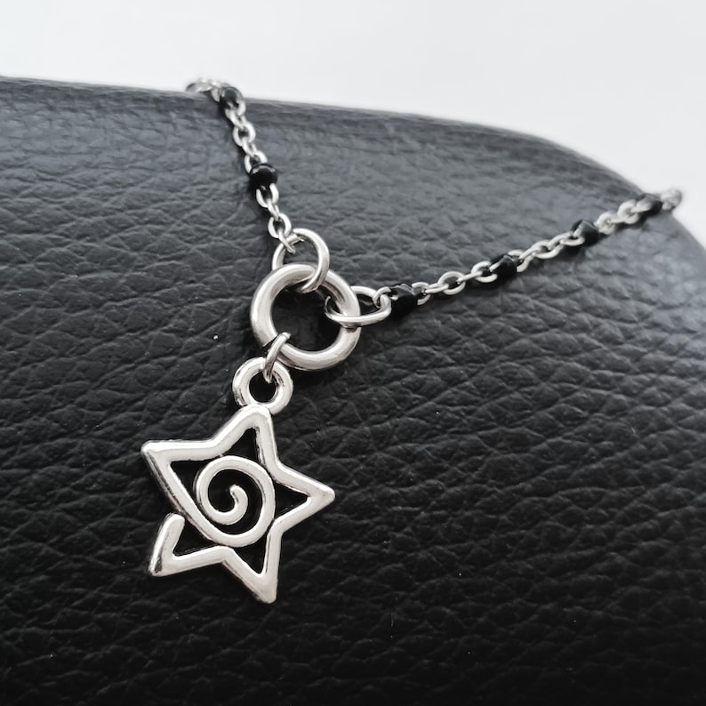 Puede incluir: Un collar de cadena de plata con un acento de cuentas negras y un dije de estrella con un dise&ntilde;o en espiral.