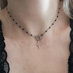Puede incluir: Un collar de cadena plateada con cuentas negras y un colgante de estrella plateada.