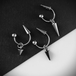 May include: Three pairs of silver-toned earrings with a curved bar design. Each earring features a small ball, a cone-shaped spike, and a curved bar. One pair has a black spike.