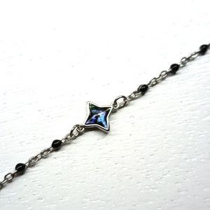 May include: A silver chain bracelet with black beads and a star-shaped charm with an iridescent blue and green center.