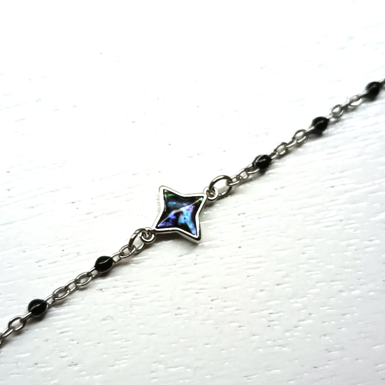 May include: A silver chain bracelet with black beads and a star-shaped charm with an iridescent blue and green center.
