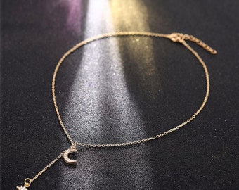 Könnte beinhalten: Eine goldene Kettenkette mit einem Halbmond-Anhänger und einem Stern-Anhänger. Die Anhänger sind mit kleinen, klaren Strasssteinen verziert.