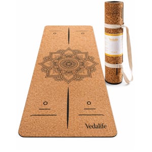 May include: A light brown cork yoga mat featuring a black mandala print in the centre, alignment lines, and the text Vedalife. A rolled version of the same mat is positioned to the right, secured with a white carrying strap and a paper label.