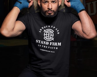 Puede incluir: Camiseta negra con el texto "ARMOUR UP AND STAND FIRM IN THE FAITH" y un gráfico de pez dentro de una cruz. La persona lleva vendas azules en las manos y pantalones cortos negros, sosteniendo una bolsa de camuflaje.