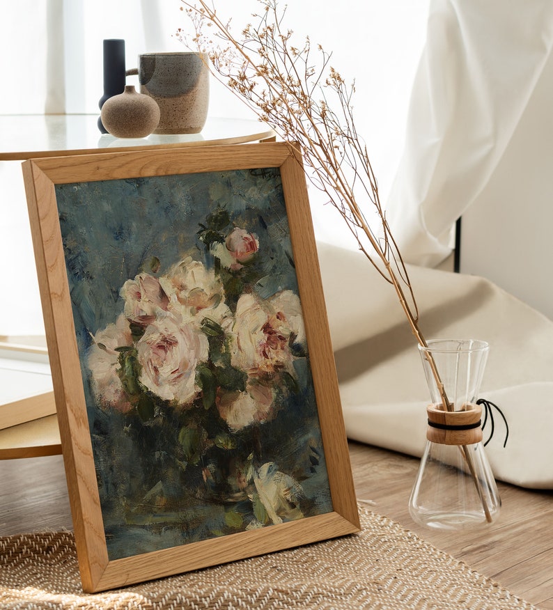 May include: A framed painting of a bouquet of white roses in a vase, with a blue background. The painting is in a wooden frame and is sitting on a table.