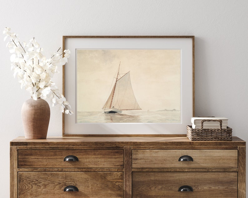 May include: A framed watercolor painting of a sailboat with white sails on a calm sea. The painting is in a light wood frame and is hanging on a wall above a wooden dresser.