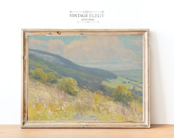 May include: A vintage landscape painting in a light wood frame. The painting depicts a rolling green hillside with a distant valley and a hazy sky. The colors are soft and muted, with shades of green, blue, and yellow.