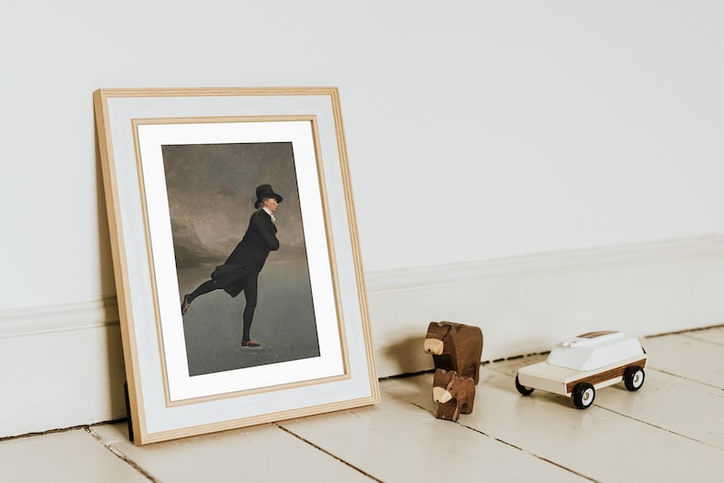 Op de afbeelding: Een ingelijst schilderij van een man in een zwarte jas en hoge hoed die schaatst op een bevroren meer. Het schilderij is in een gouden lijst met een witte passe-partout.