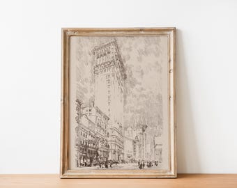 May include: A framed black and white line drawing of a tall building in a city. The building is surrounded by other buildings and people walking on the street. The drawing is on a beige background.