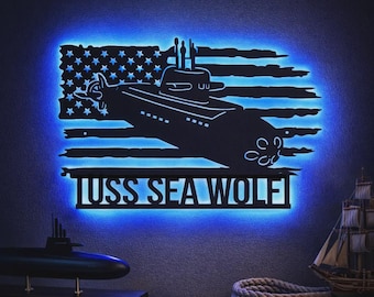 Puede incluir: Un letrero de pared de metal negro con la silueta de un submarino superpuesta sobre un diseño de bandera estadounidense desgastada. El letrero está retroiluminado con un brillo LED azul intenso y muestra el texto USS SEA WOLF en mayúsculas.