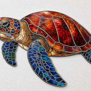 Könnte beinhalten: Eine Wanddekoration aus Buntglas in Form einer Meeresschildkröte mit einem Panzer in tiefen Rot- und Orangetönen, einem Kopf in Blau- und Bernsteinfarben sowie Flossen aus irisierenden blauen und grünen Glasstücken mit dunklen Metallnähten.