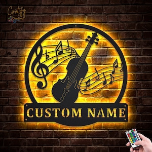 May include: A black metal wall art piece featuring a violin with musical notes and a treble clef. The art piece is illuminated with warm yellow LED lights and has a customizable nameplate that reads "CUSTOM NAME".