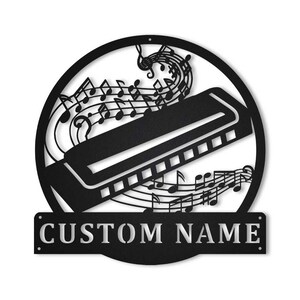 Può includere: Arte da parete in metallo nero con un'armonica con note musicali che scorrono intorno ad essa. L'opera d'arte include il testo "CUSTOM NAME".