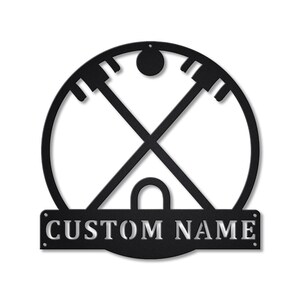 Könnte beinhalten: Schwarze Wandkunst aus Metall mit einem stilisierten Design eines Kreises mit gekreuzten Linien und einem kleinen Kreis oben. Das Design erinnert an ein indianisches Symbol. Der untere Teil des Kunstwerks hat ein rechteckiges Banner mit dem Text "CUSTOM NAME".
