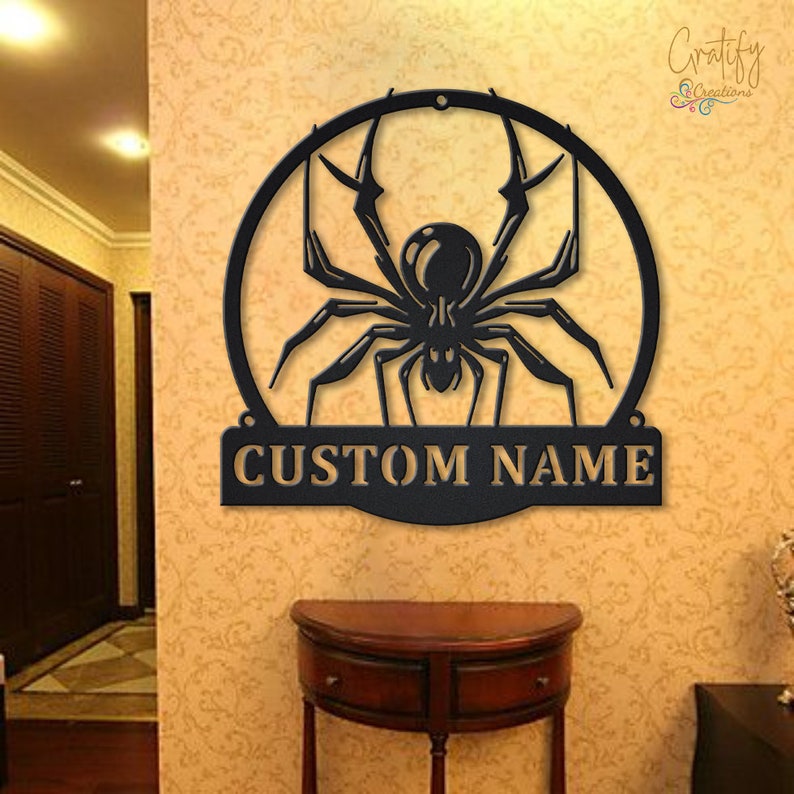Może przedstawiać: Czarna metalowa ozdoba ścienna przedstawiająca pająka w k&oacute;łku z napisem "CUSTOM NAME" poniżej.