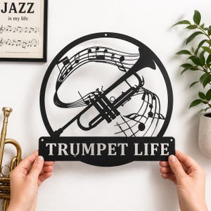 Puede incluir: Arte de pared de metal negro con una trompeta y notas musicales dentro de un marco circular. Las palabras "TRUMPET LIFE" se muestran en una placa rectangular debajo de la trompeta. Un marco "JAZZ is my life" es visible en el fondo.