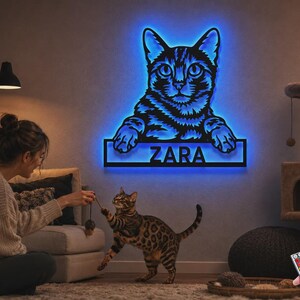 May include: A wall-mounted cat-shaped sign featuring a black silhouette of a cat with glowing blue LED backlighting. The design includes a rectangular nameplate at the bottom with the name ZARA in bold, capital letters, illuminated in blue.