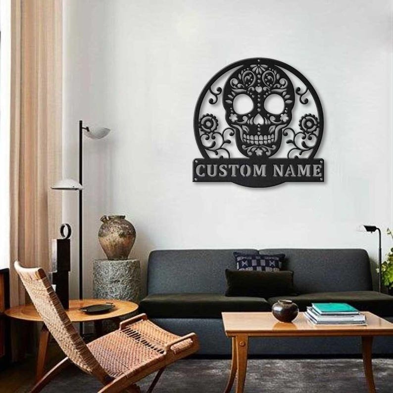 May include: Black metal wall art featuring a detailed skull design within a circular frame, with floral accents. The text "CUSTOM NAME" is displayed on a rectangular plaque below the skull. This decorative piece is suitable for interior decor.