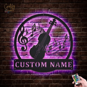May include: A black metal wall art piece featuring a violin with musical notes and a treble clef. The art is illuminated with purple LED lights and has a custom nameplate that reads "CUSTOM NAME".