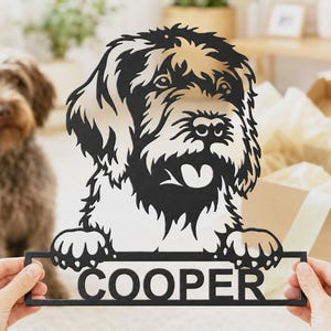 May include: A black metal wall art piece featuring a stylized portrait of a shaggy dog with its paws resting on a rectangular frame. The name COOPER is cut out in bold, capital letters within the frame, creating a decorative sign for home display.