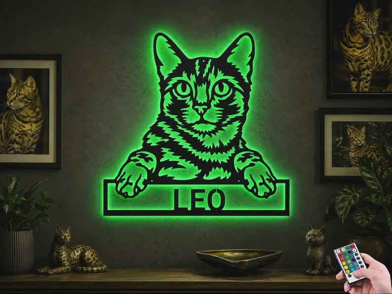 May include: A wall-mounted cat-shaped sign featuring a black silhouette of a cat with green LED backlighting. The cat is resting its paws on a rectangular frame that contains the name LEO in bold, cut-out capital letters, illuminated in green.