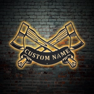 May include: A metal sign with two crossed axes and a banner that says "CUSTOM NAME". The sign is illuminated with a warm yellow light and is set against a brick wall.