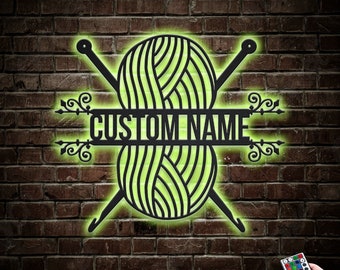 Pode incluir: Uma placa de metal preta com fio e agulha de crochê com o texto "CUSTOM NAME" no centro. A placa é iluminada com um brilho verde e é montada em uma parede de tijolos. Um controle remoto é visível no canto inferior direito.