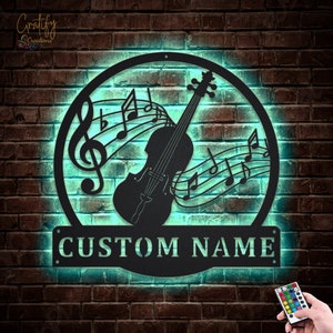 May include: A black metal wall art design featuring a violin with musical notes and a treble clef. The design is illuminated with a teal light and has a space for a custom name. The name "CUSTOM NAME" is displayed on the sign.