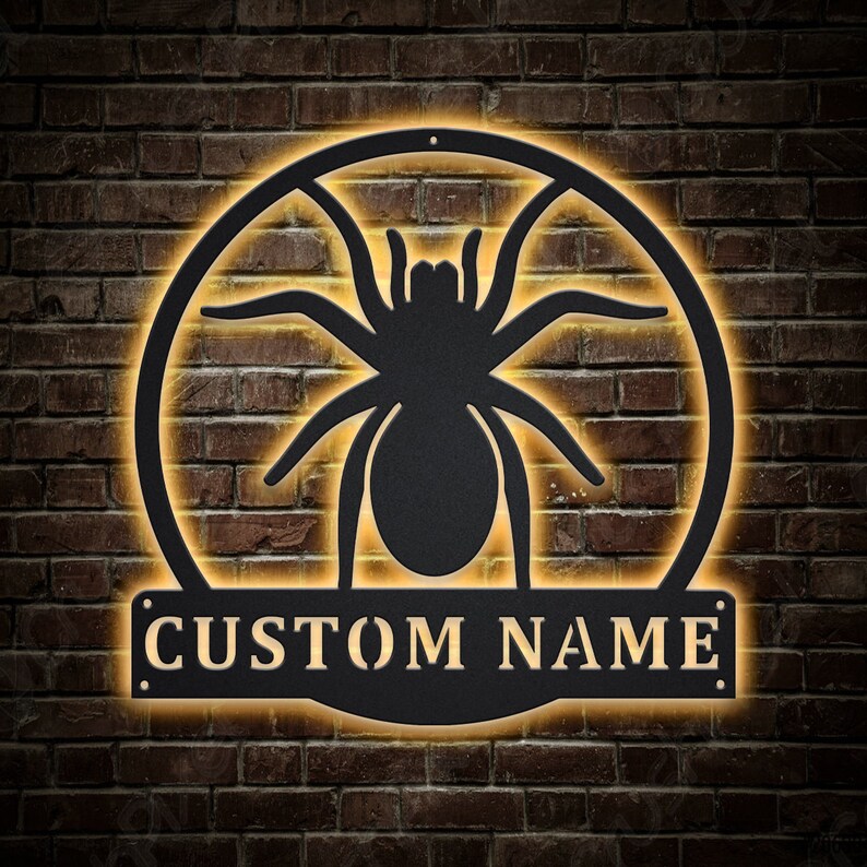 May include: Black metal spider silhouette with a custom nameplate that reads "CUSTOM NAME" in a gold font. The spider is in a circle with a glowing yellow halo.