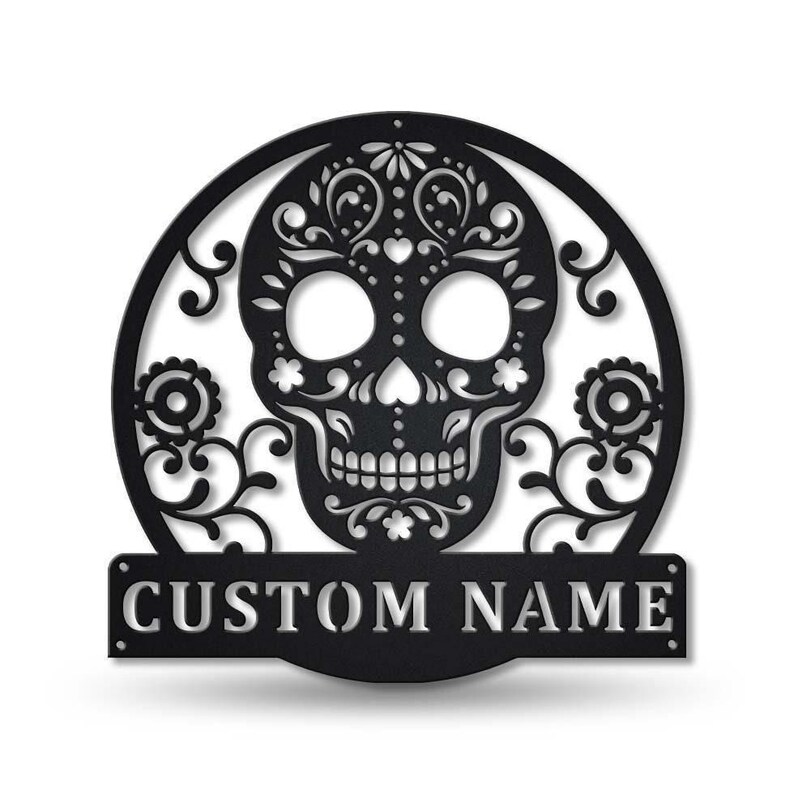 May include: Black metal Day of the Dead skull wall art. The skull is intricately designed with floral patterns and set within a circular frame. The words "CUSTOM NAME" are displayed on a rectangular banner below the skull.